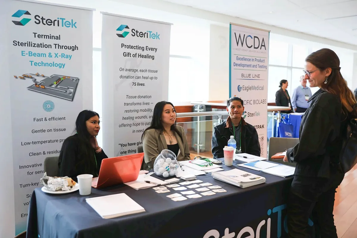 Three Steri-Tek representatives sit at their table beneath company banners and talk with an attendee standing in front of them.