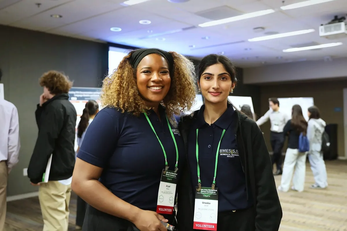 Two smiling student volunteers pose together at the poster session.