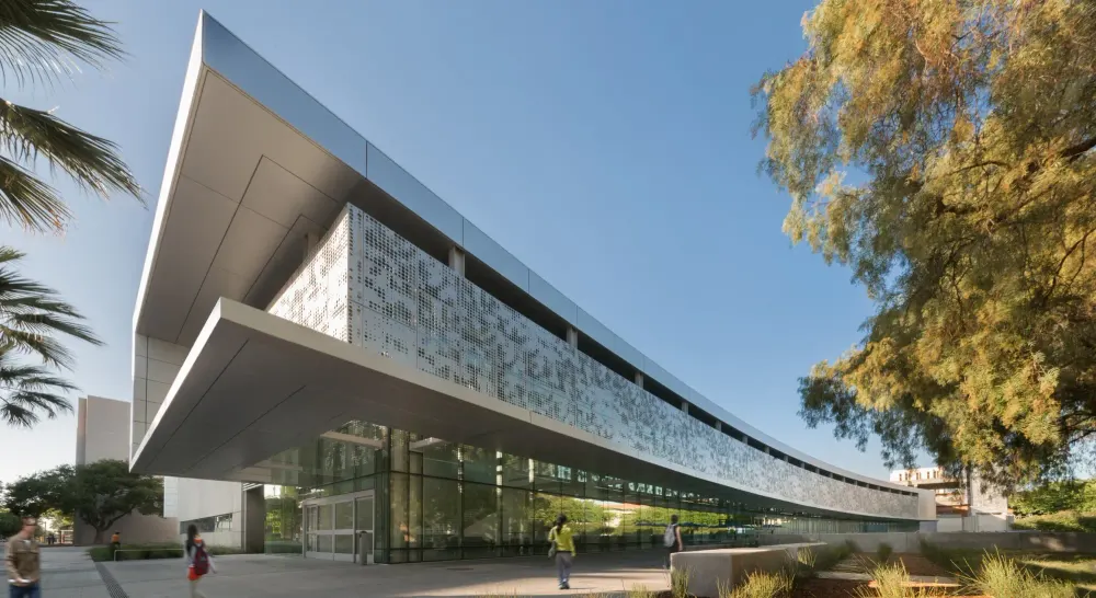 The curved exterior of the SJSU Student Union, with a perforated metal facade above a glass ground floor, as students walk past.